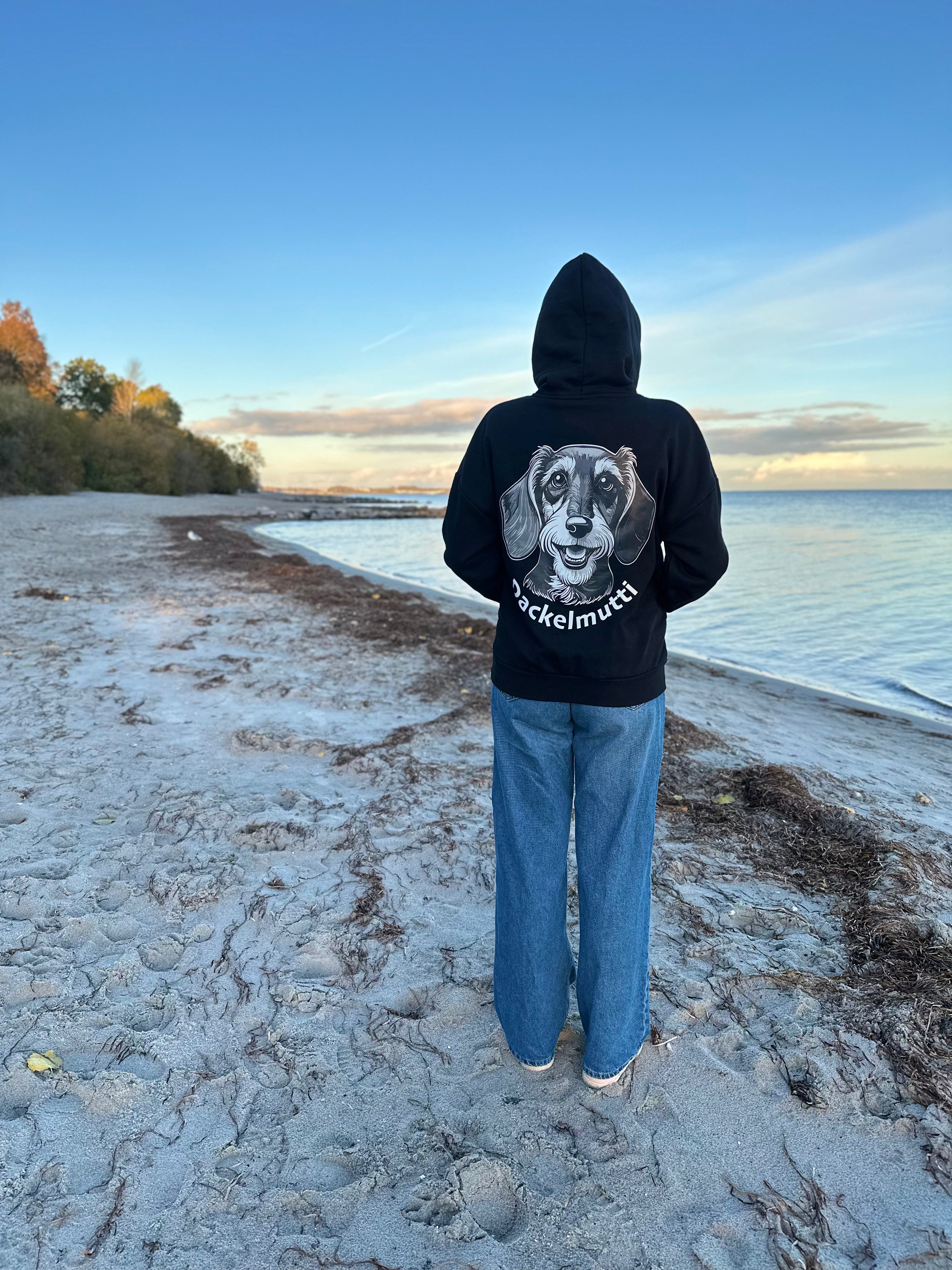 Moderner Oversized-Hoodie in der Rückansicht am Strand mit einem großen Print-Motiv eines Dackelkopfes und dem geschwungenen Schriftzug Dackelmutti.